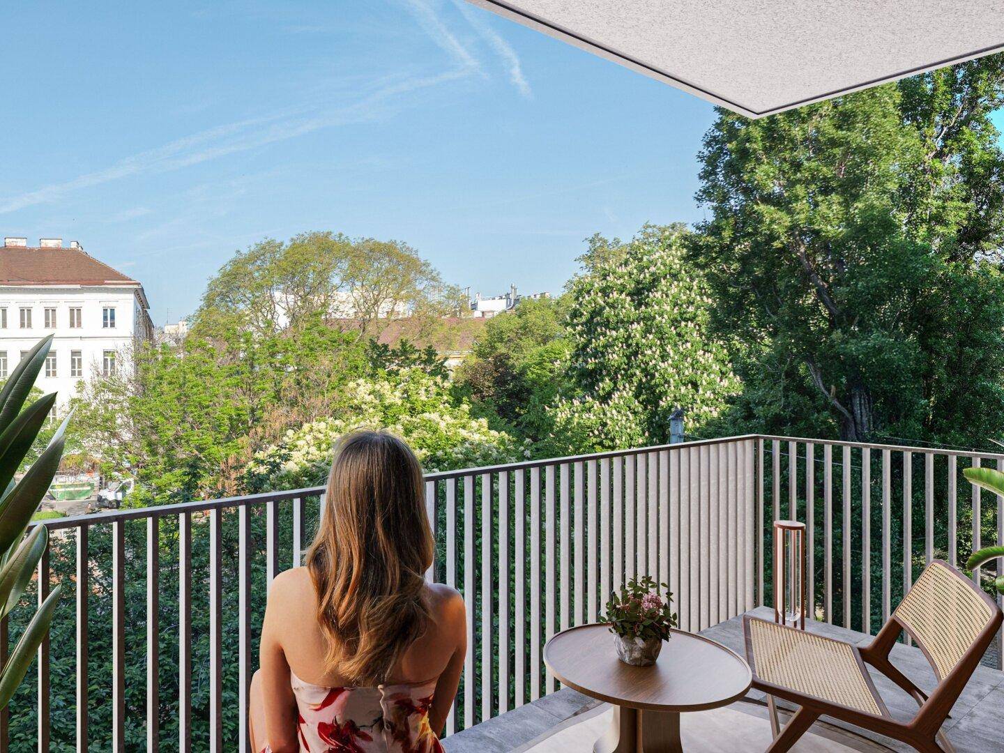 Sonnenverwöhnter Balkon mit modernen Möbeln und weitem Blick über grüne Baumwipfel und Gebäude.