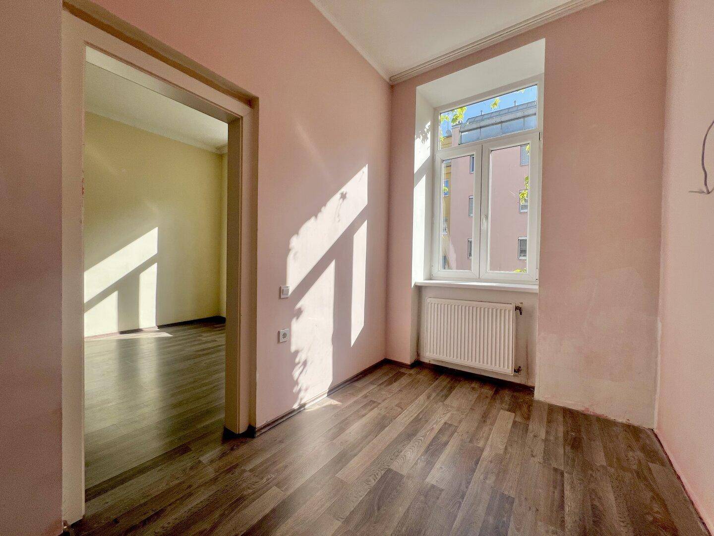 Lichtdurchflutetes Zimmer mit Holzboden und Blick auf die umliegenden Gebäude.
