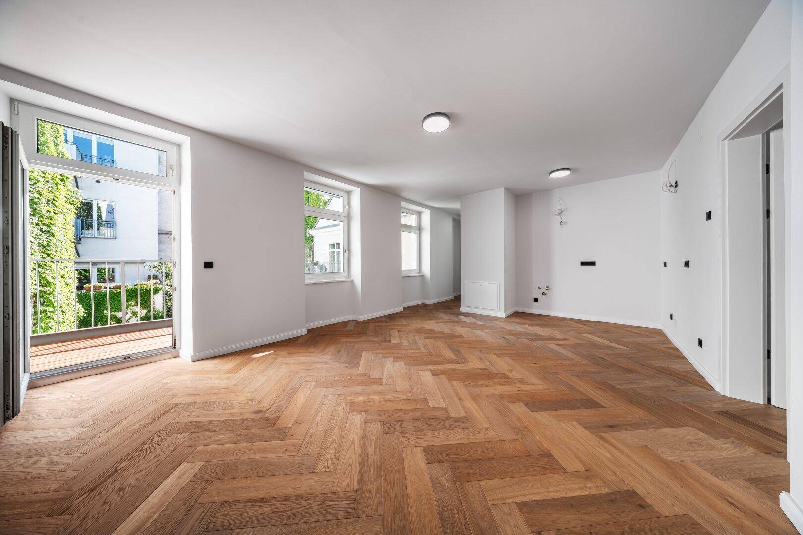 Heller Raum mit elegantem Fischgrätparkett und Zugang zu einem kleinen Balkon.