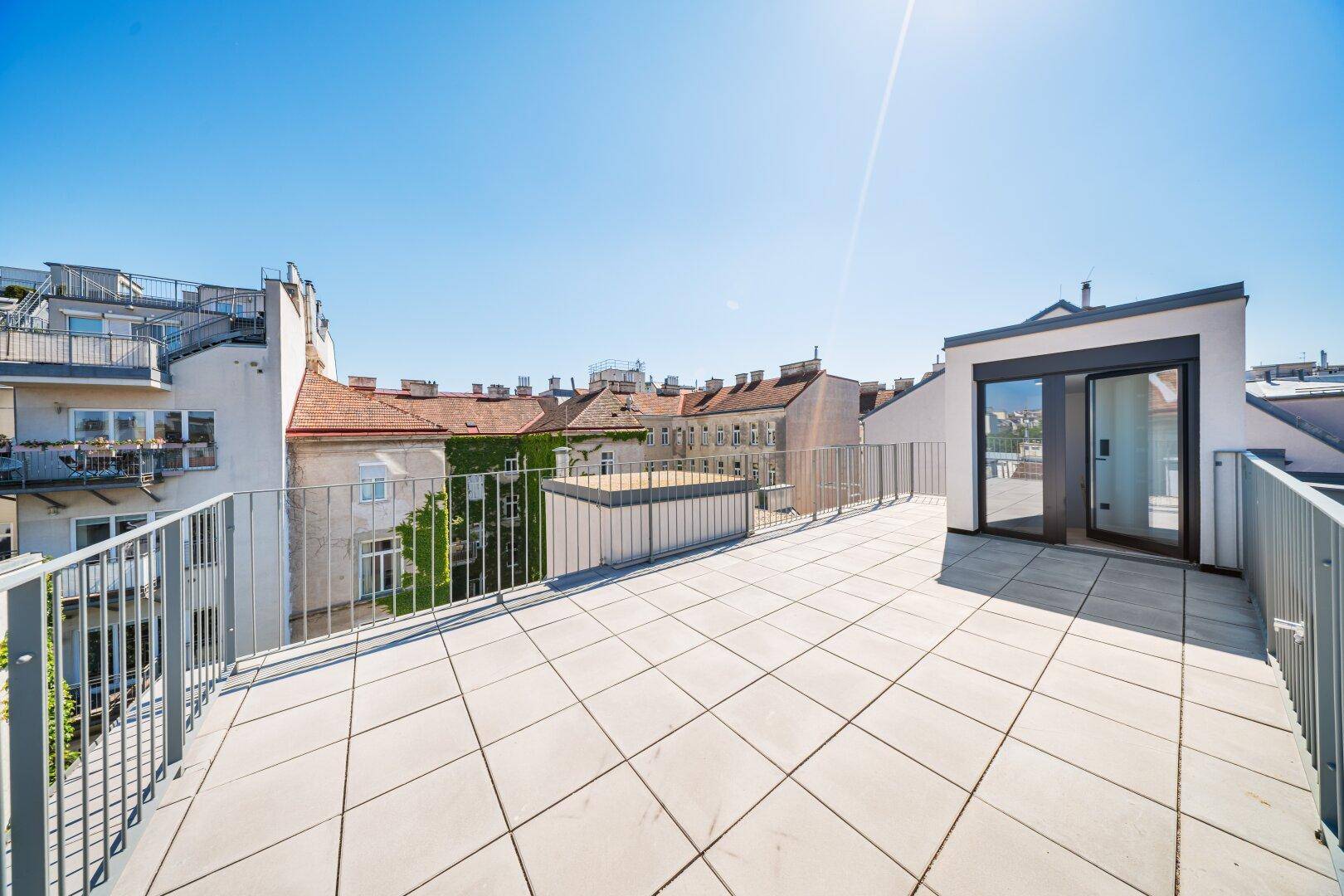 Geräumige Dachterrasse mit Fliesenboden, Metallgeländer und weitem Blick über die Stadt.