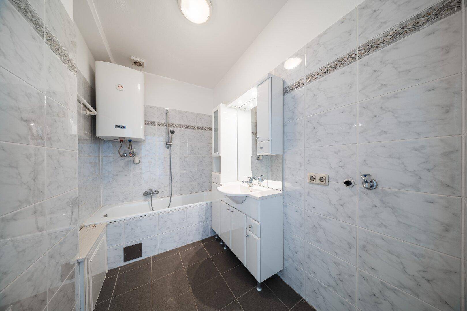 Gefliestes Badezimmer mit Badewanne, Dusche und Waschbeckenunterschrank.