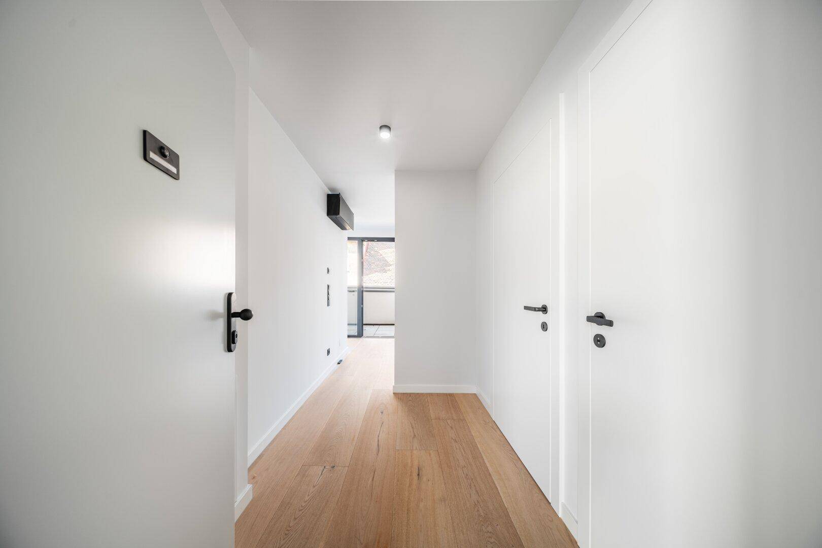 Heller Flur mit Holzboden und weißen Türen, der zu weiteren Räumen der Wohnung führt.