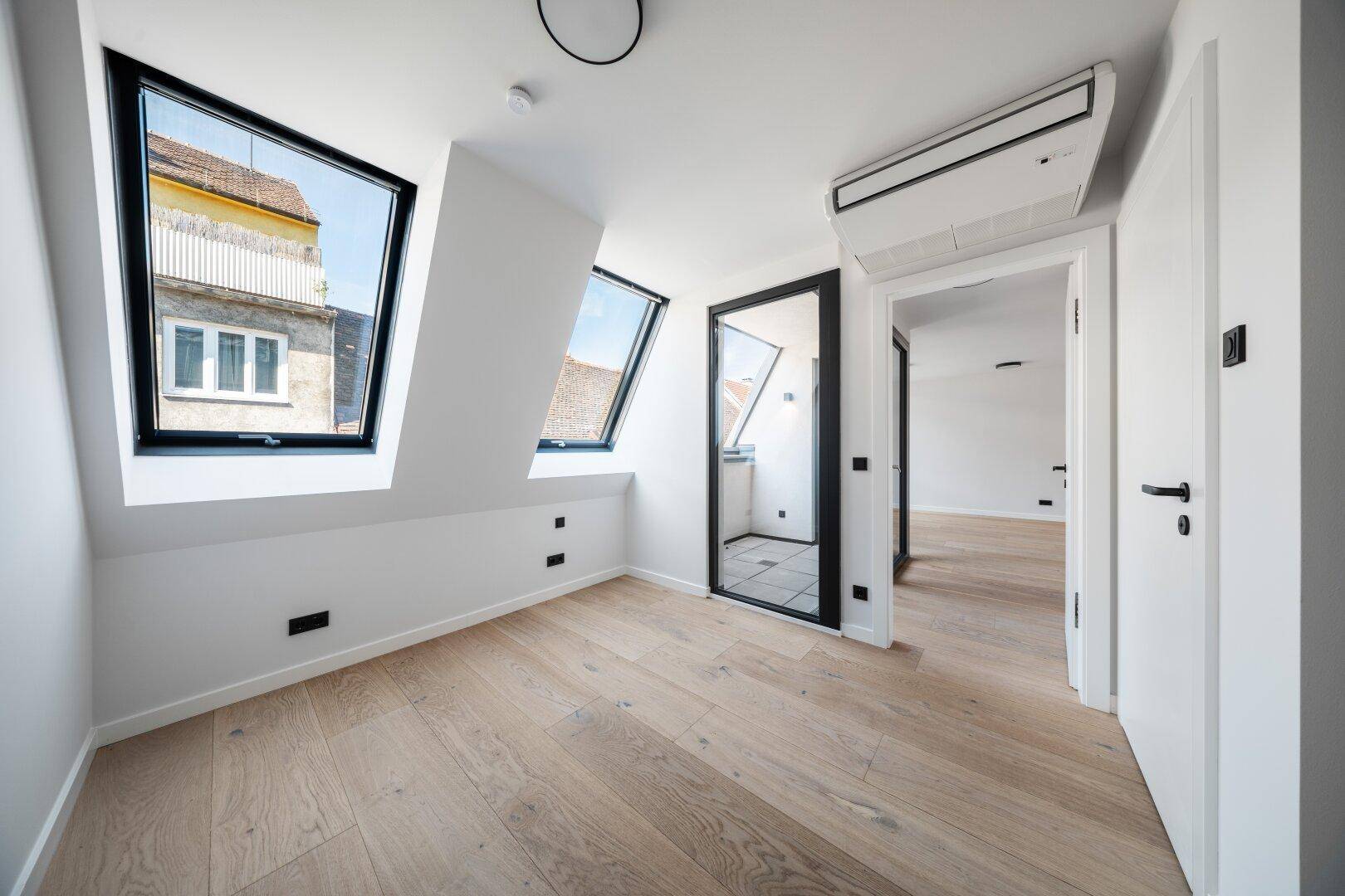 Modernes Schlafzimmer im Dachgeschoss mit Holzboden, Klimaanlage und Zugang zu einem weiteren Bereich.