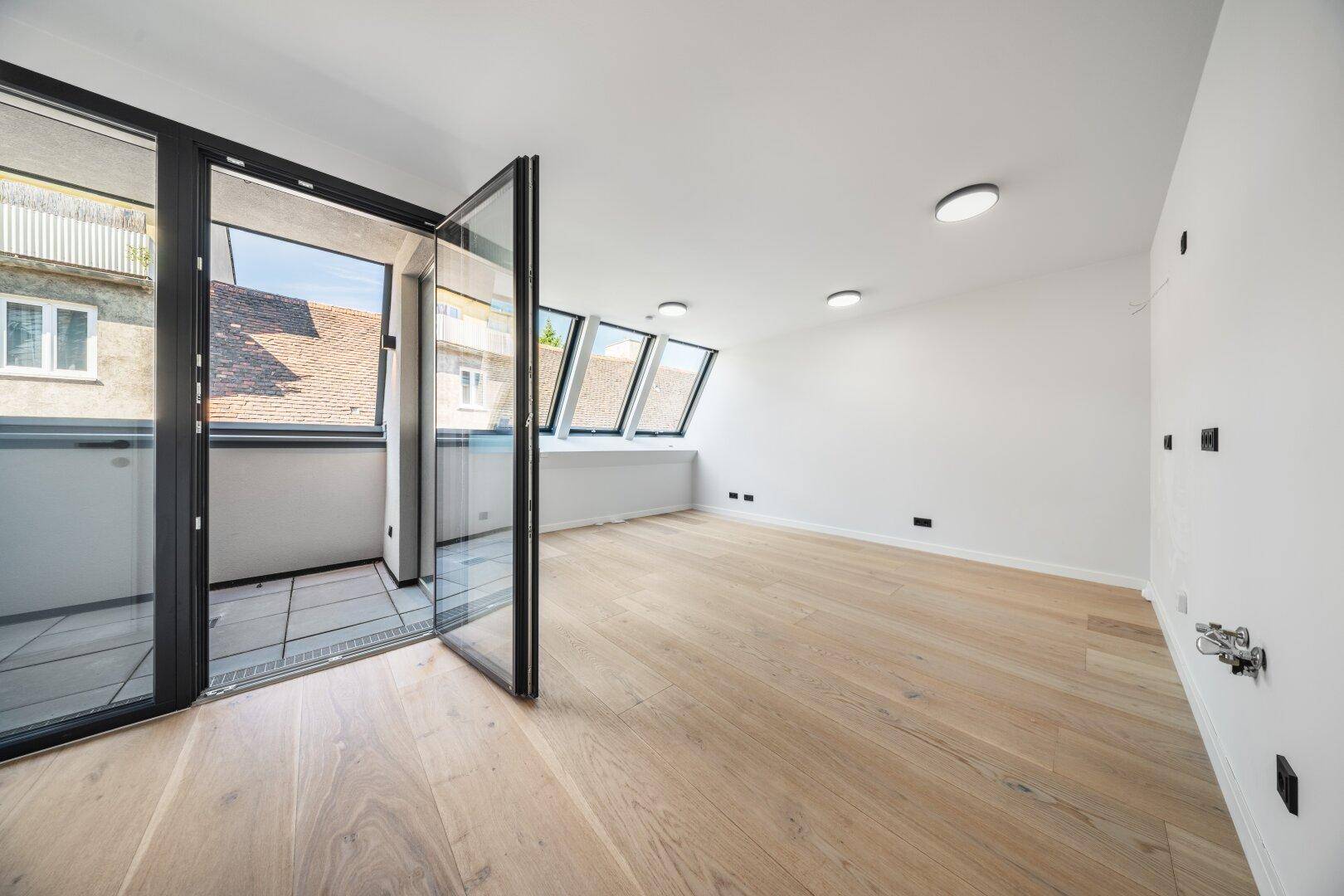 Helles Schlafzimmer mit Holzboden, Dachfenstern und direktem Zugang zu einem kleinen Balkon.