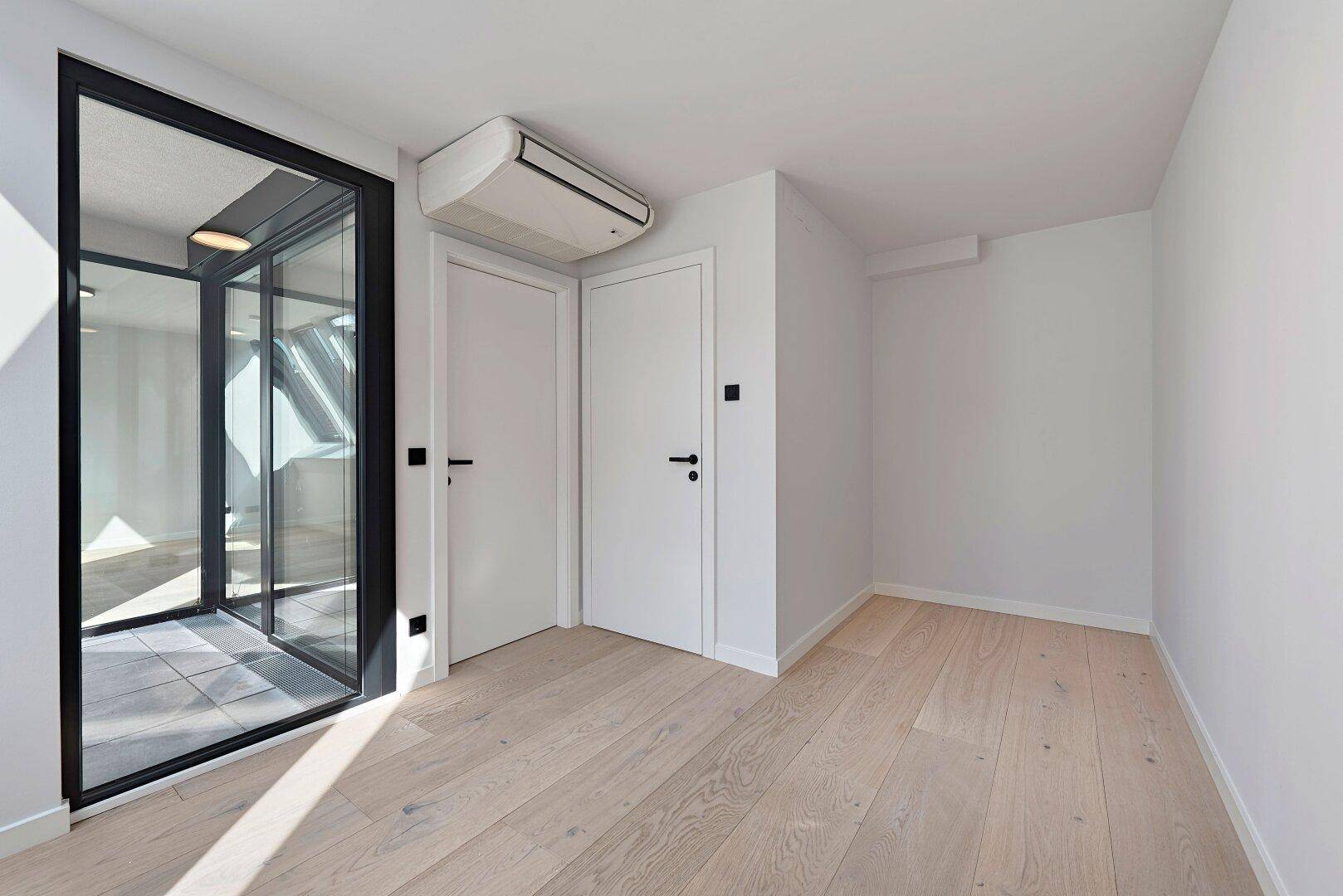 Geräumiges Schlafzimmer mit Holzboden, Klimaanlage und Zugang zu einem verglasten Bereich.
