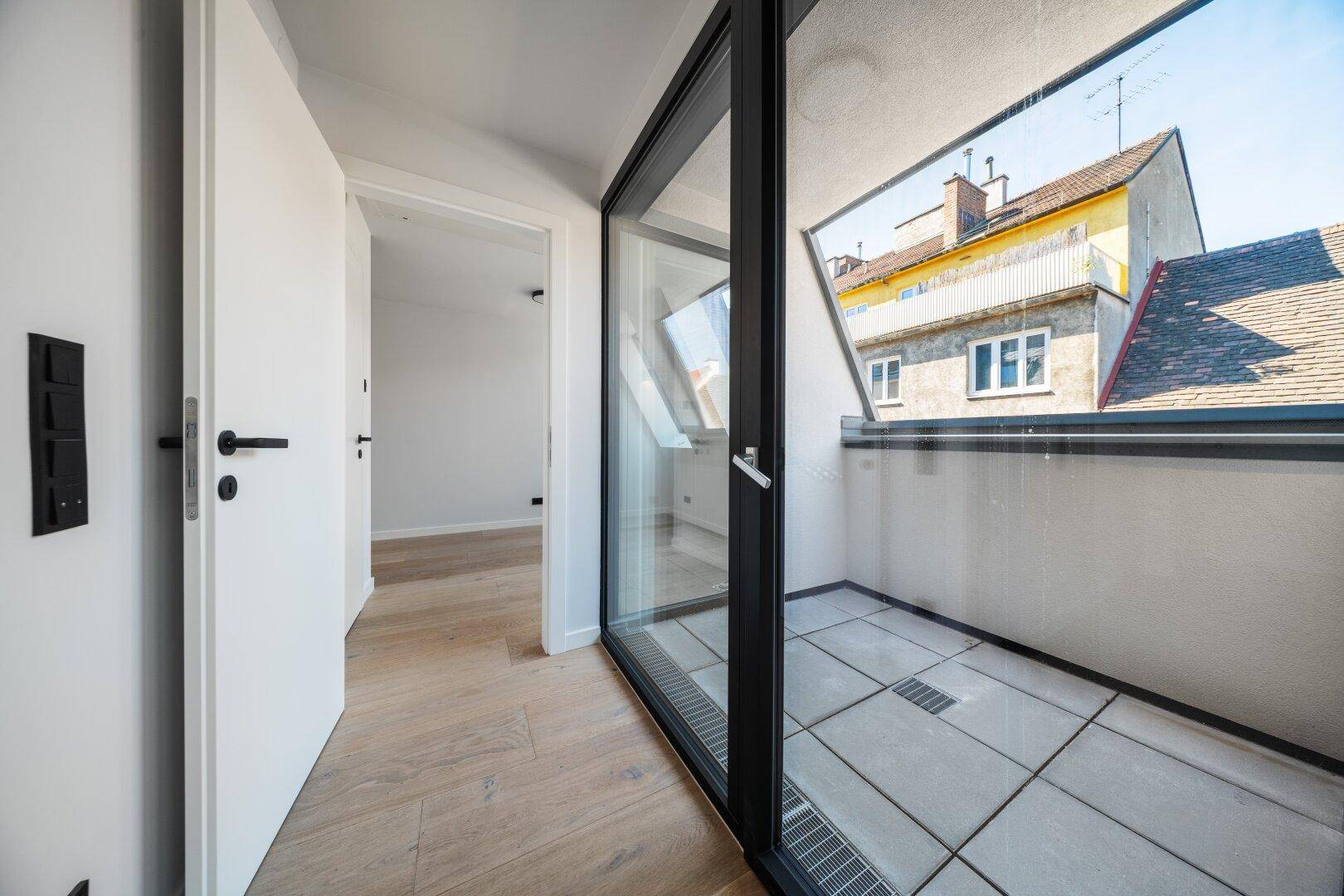 Heller Flur mit Holzboden und direktem Zugang zu einem kleinen Balkon mit Stadtblick.