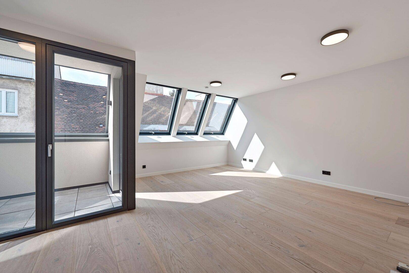 Lichtdurchflutetes Schlafzimmer mit Holzboden, Dachfenstern und Balkonzugang in modernem Stil.
