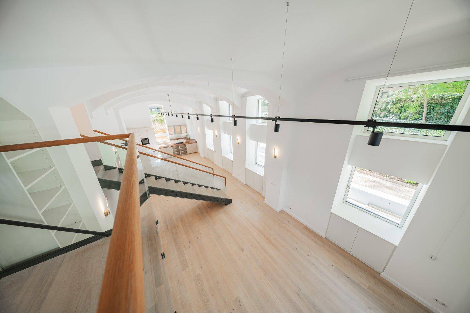 Blick von der oberen Ebene in den offenen Wohnbereich mit moderner Treppe und hohen Gewölbedecken.