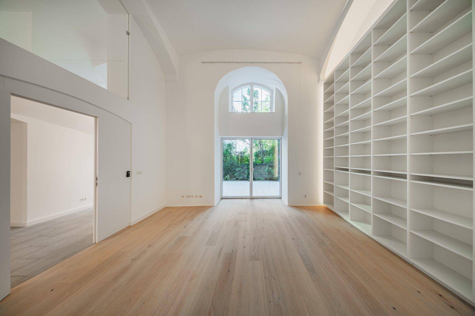 Helles, geräumiges Wohnzimmer mit hohen Gewölbedecken, Holzboden und einer großen Bücherwand.