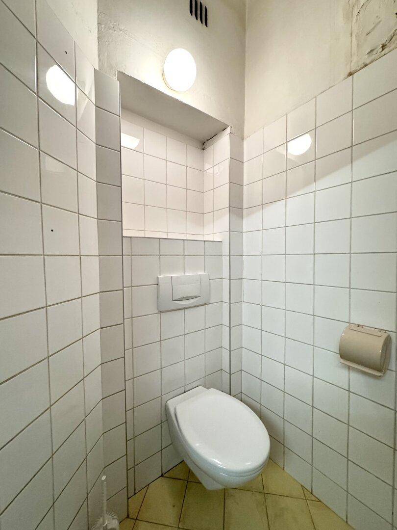 Einfache, weiß geflieste Toilette mit wandhängendem WC, funktional und gut erhalten.