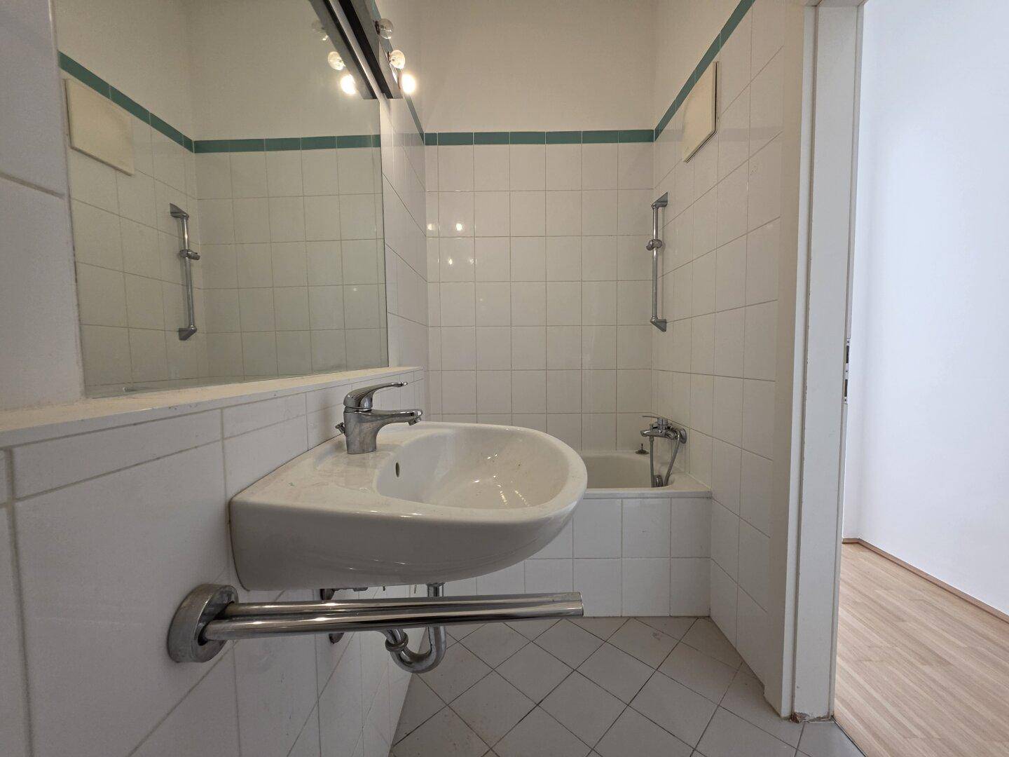 Badezimmer mit weißen Fliesen, Waschbecken und einer Badewanne, in gutem Zustand.