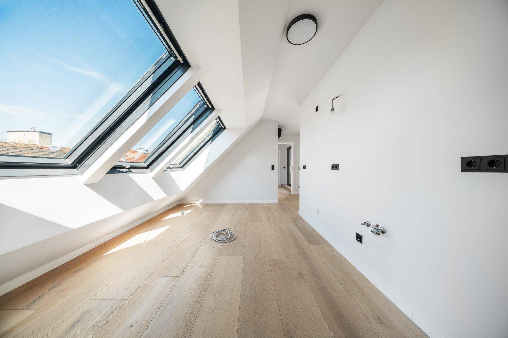 Lichtdurchfluteter Raum im Dachgeschoss mit Holzboden und mehreren großen Dachfenstern.