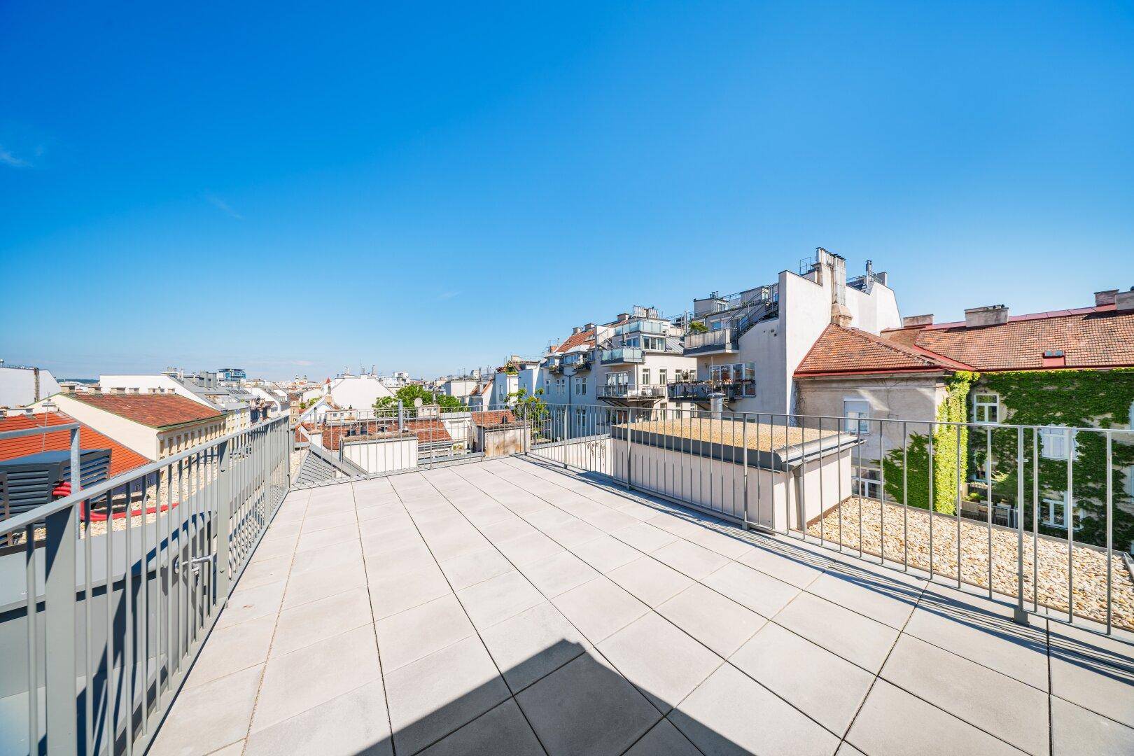 Weitläufige, unmöblierte Dachterrasse mit Fliesenboden und Panoramablick über die Stadt.