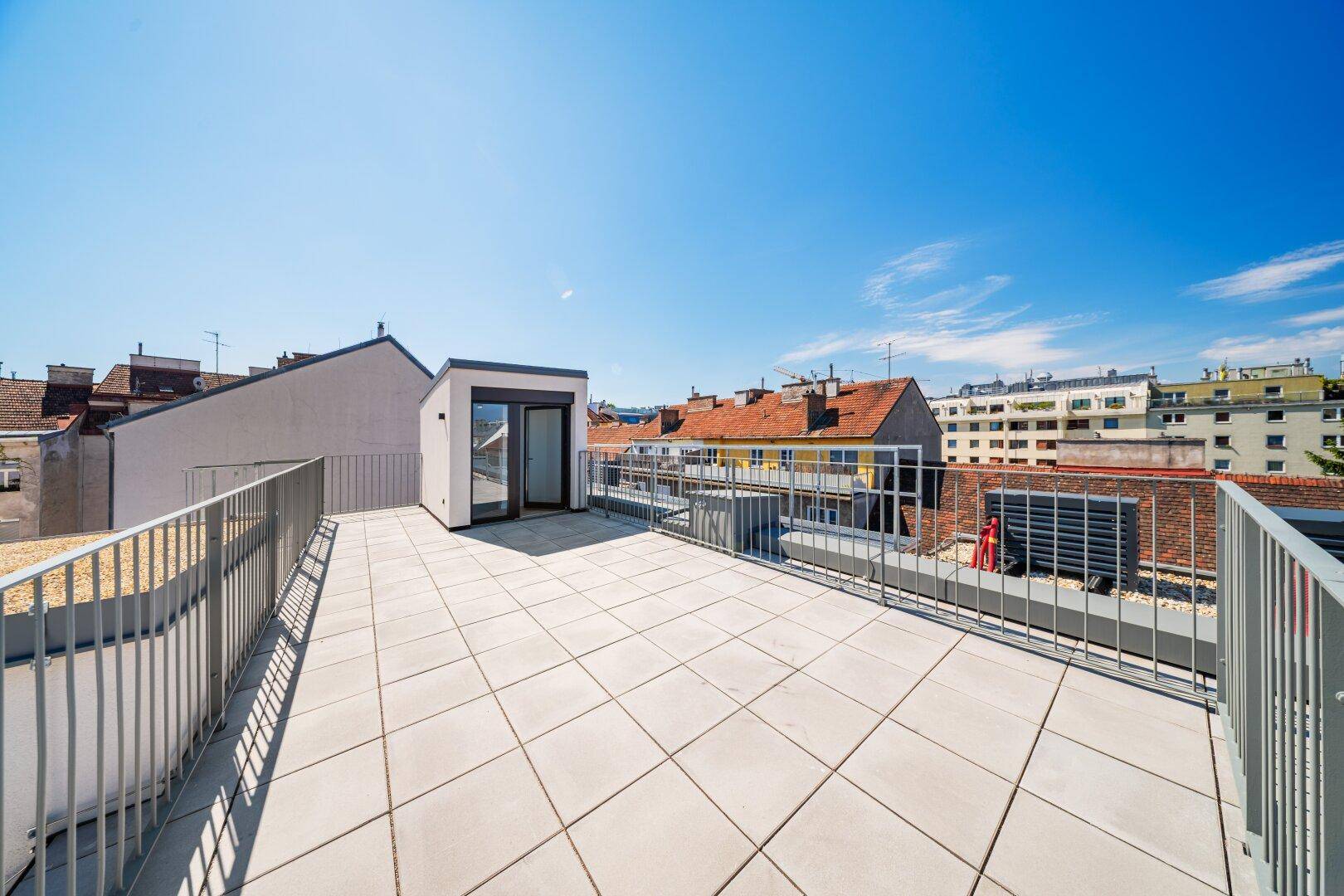 Sonnige Dachterrasse mit Fliesenboden und weitem Blick über die Dächer der Stadt.