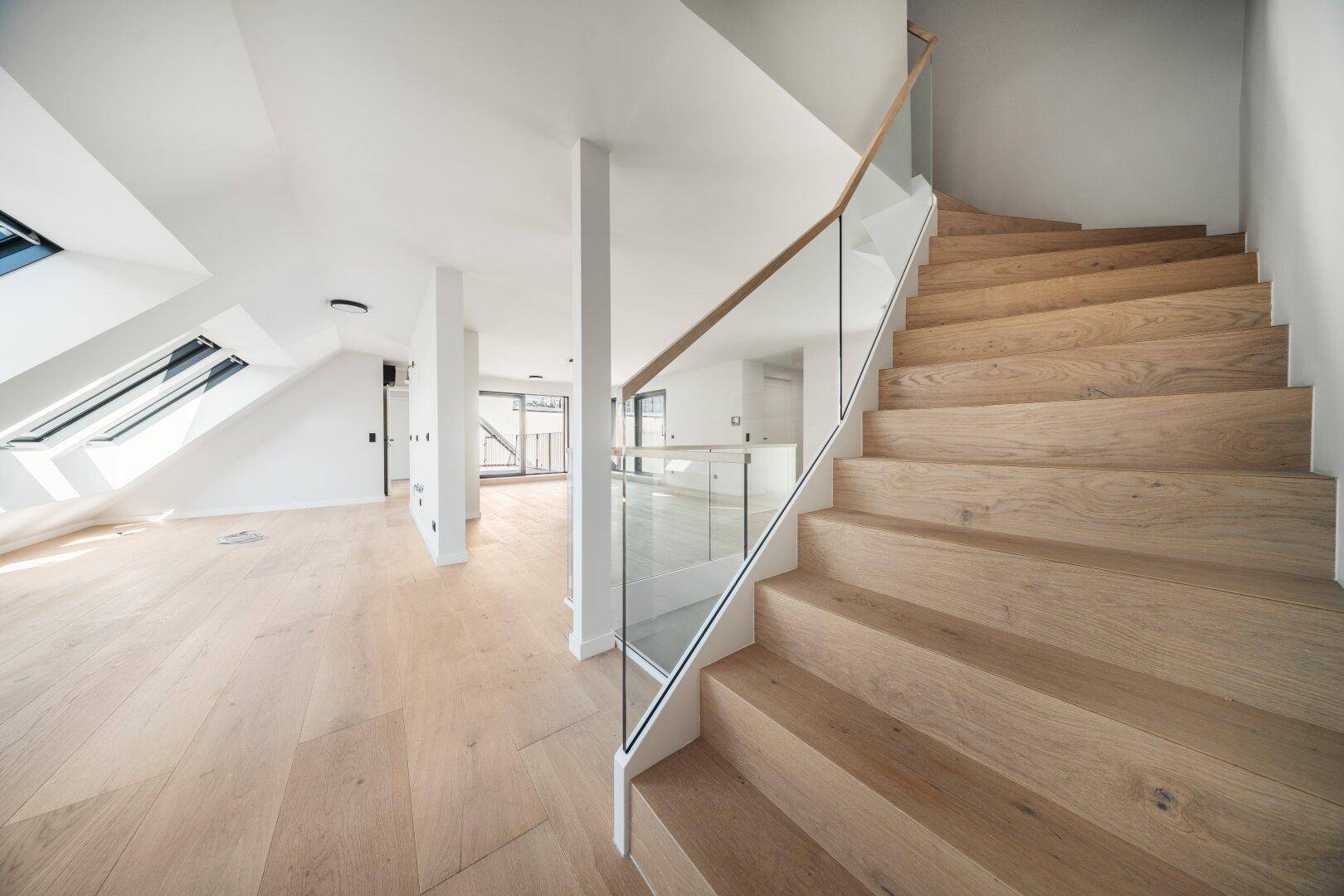 Elegante Holztreppe mit Glasgeländer in einem lichtdurchfluteten, modernen Wohnambiente.