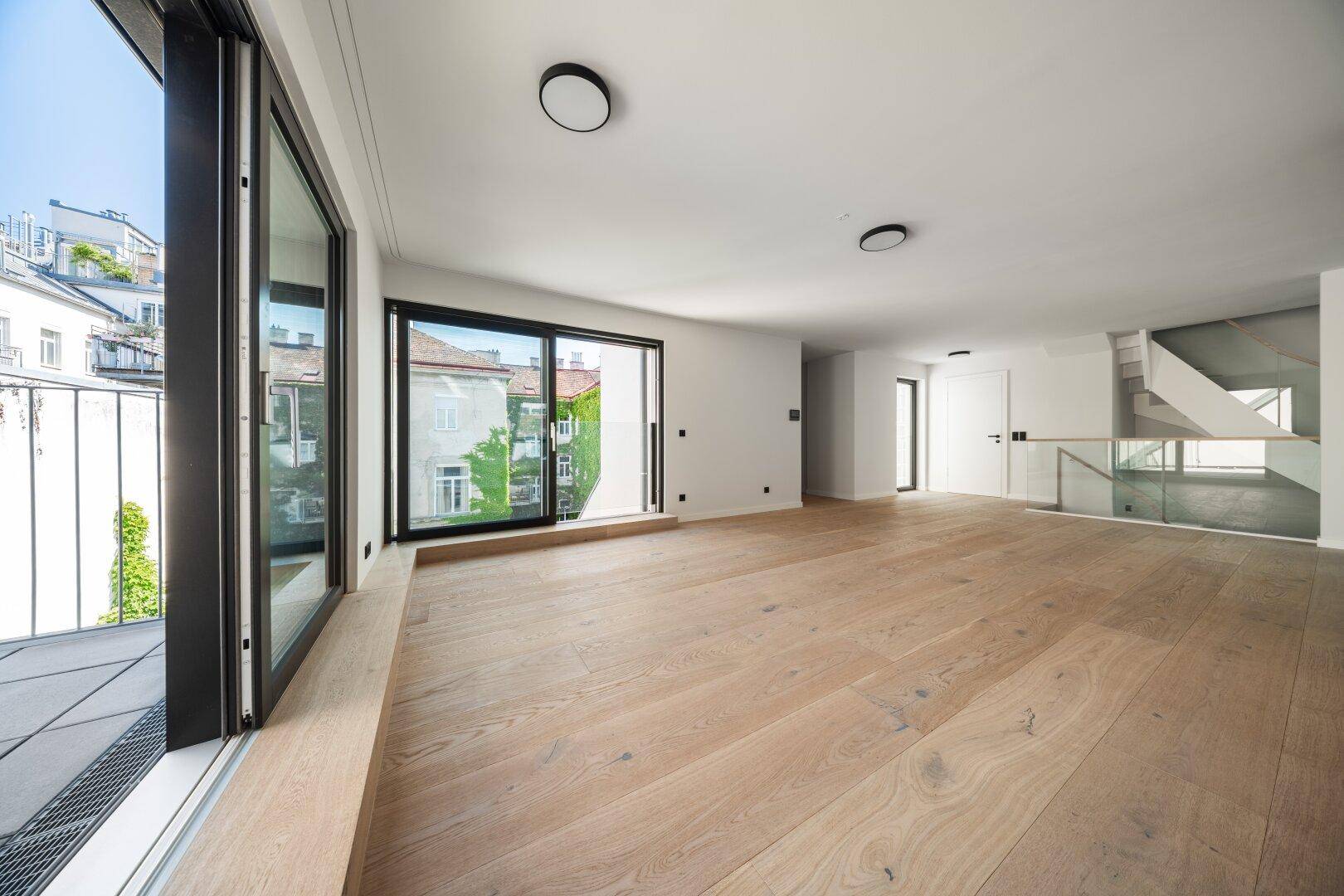 Geräumiger, heller Wohnbereich mit Holzboden, großen Schiebetüren und moderner Treppe.