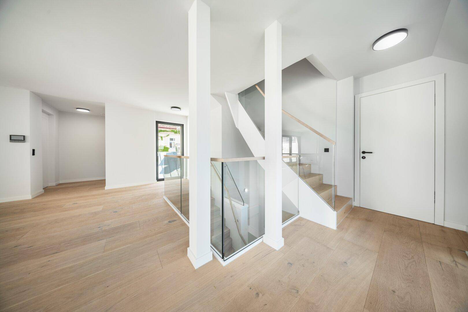 Moderne Treppe mit Glasgeländer und Holzstufen in einem hellen, offenen Eingangsbereich.