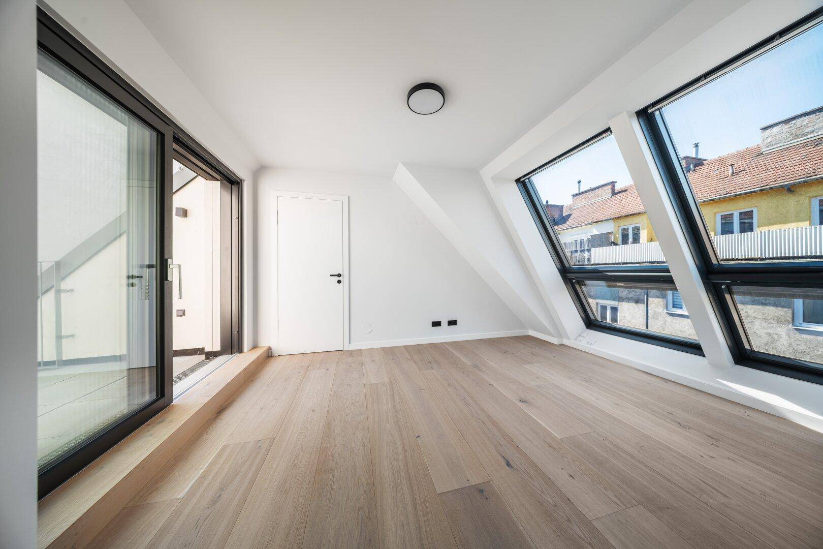 Geräumiges Dachgeschosszimmer mit Holzboden, großen Dachfenstern und Balkonzugang.