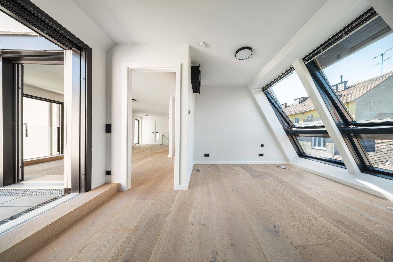 Helles Dachgeschosszimmer mit Holzboden, großen Dachfenstern und Zugang zu einem Balkon.
