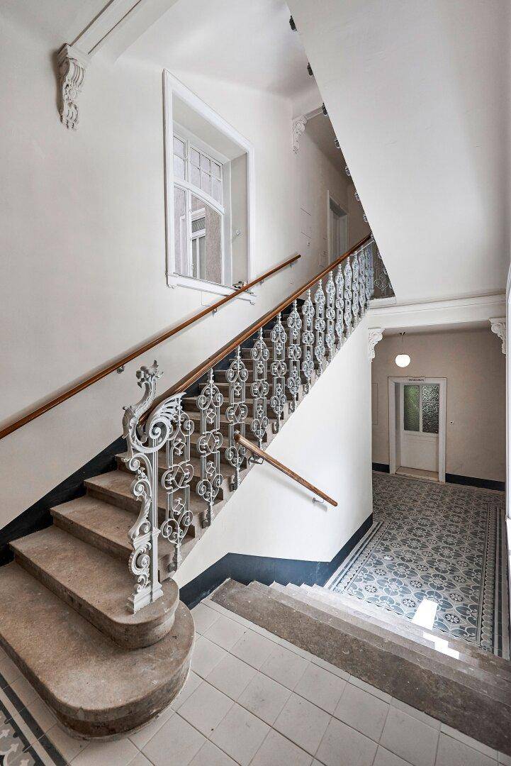 Elegantes Treppenhaus mit kunstvollem Geländer, Steinstufen und gemusterten Bodenfliesen im Eingangsbereich.