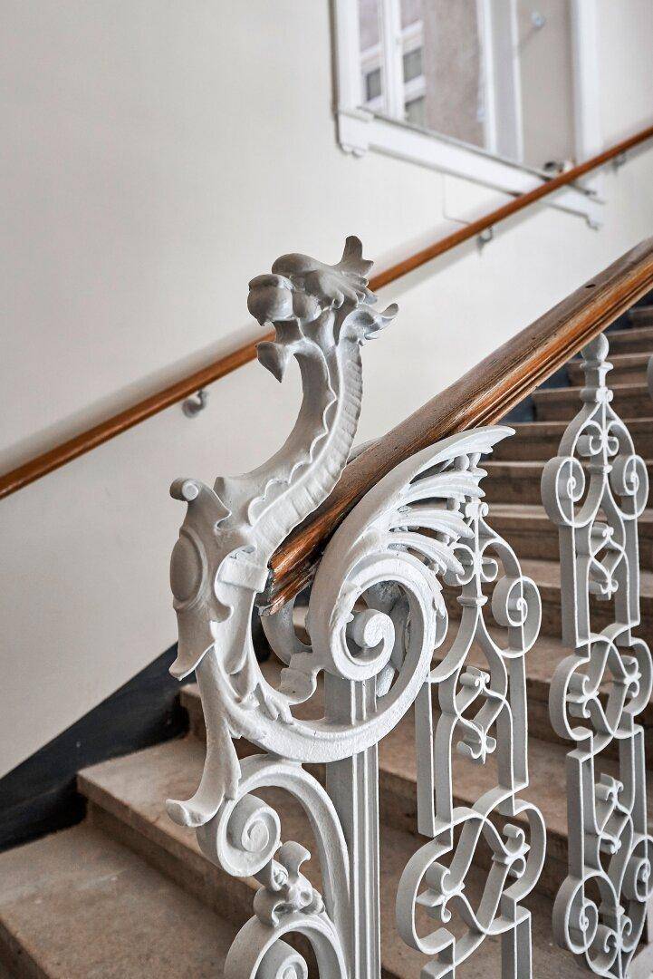 Detailaufnahme eines kunstvollen Treppengeländers mit einem dekorativen Drachenmotiv und Holzhandlauf.