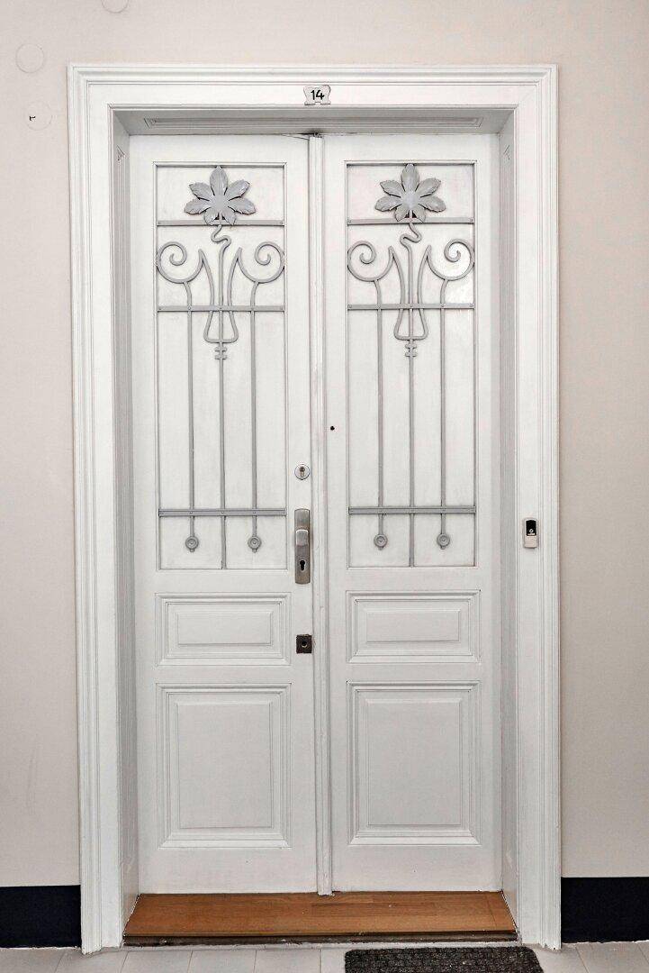 Nahaufnahme einer eleganten weißen Doppeltür mit dekorativen Metallverzierungen im oberen Bereich.