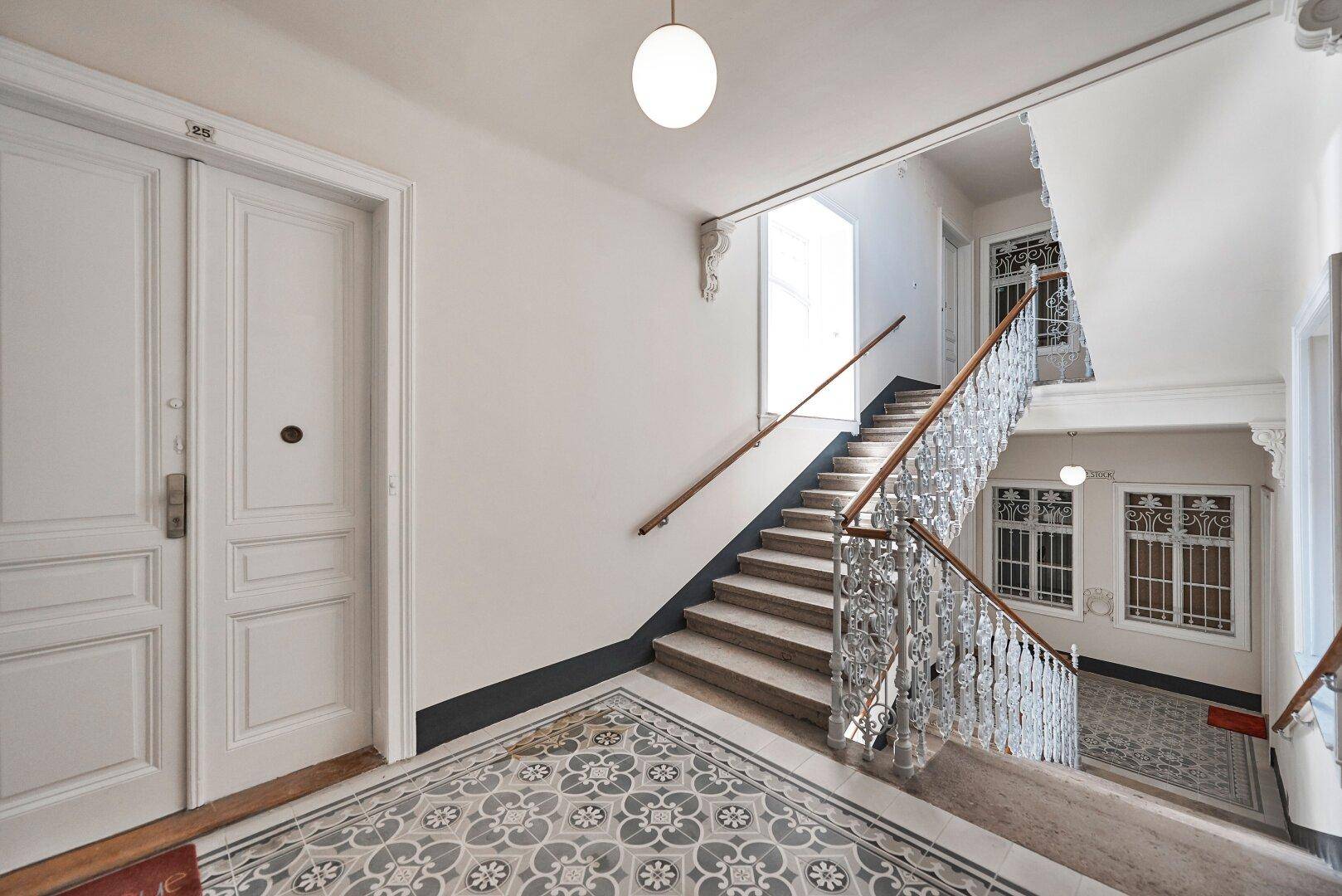 Geräumiges Treppenhaus mit kunstvollem Geländer, Steinstufen und mehreren Türen in einem Altbau.