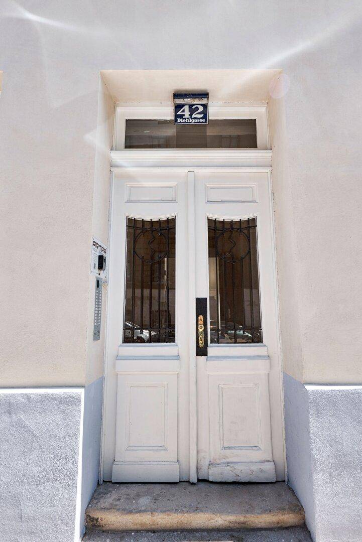 Eingangstür eines Gebäudes mit der Hausnummer 42, einer weißen Doppeltür und dekorativen Metallgittern.