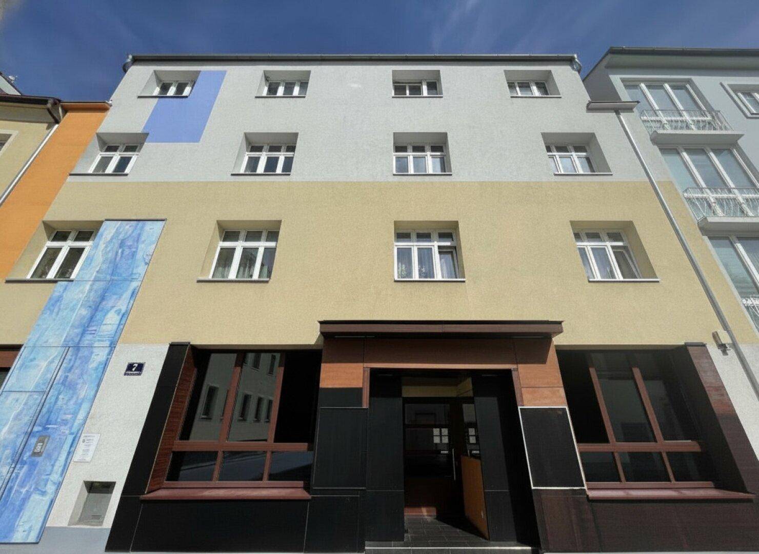 Mehrstöckiges Gebäude mit farbiger Fassade, vielen Fenstern und einem modernen Eingangsbereich.