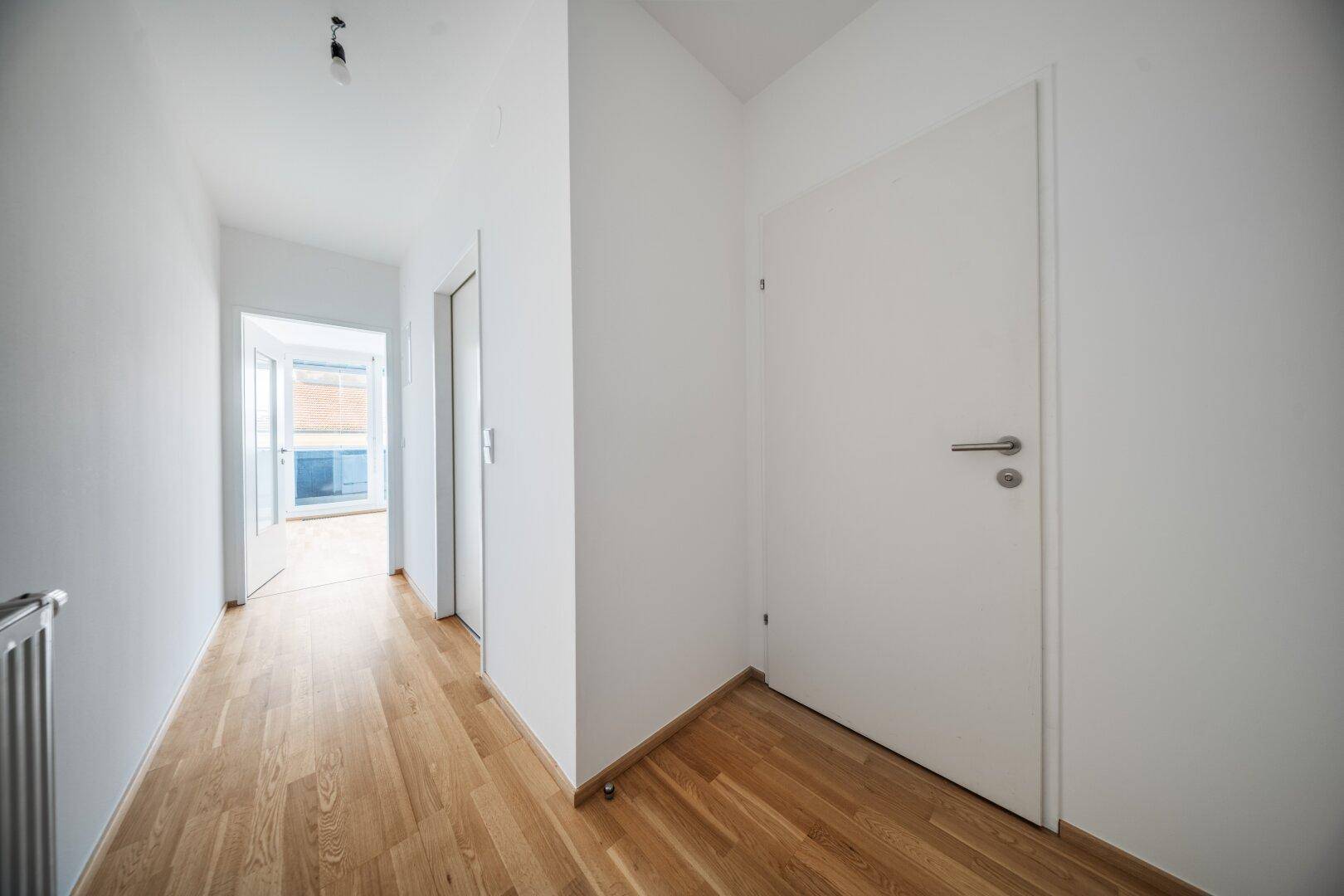 Heller Flur mit Holzboden und weißen Wänden, der zu weiteren Räumen führt.