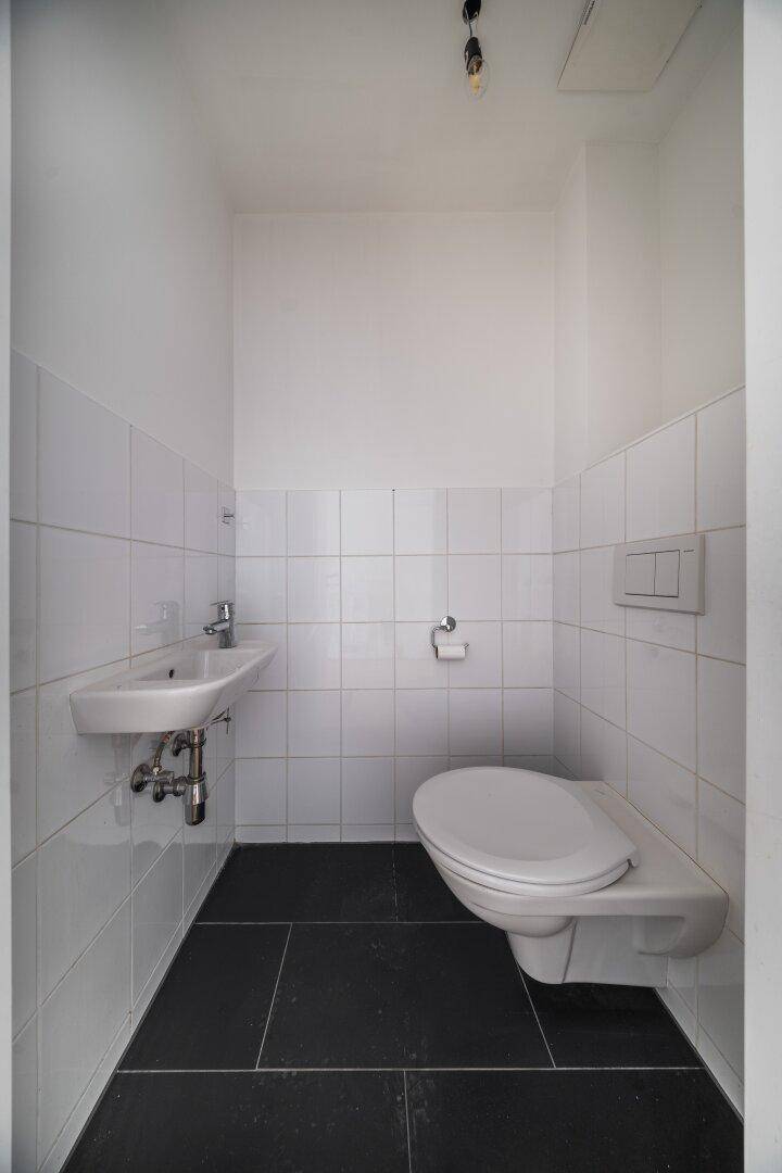 Separates Gäste-WC mit Wand-WC, kleinem Waschbecken und dunklem Fliesenboden.