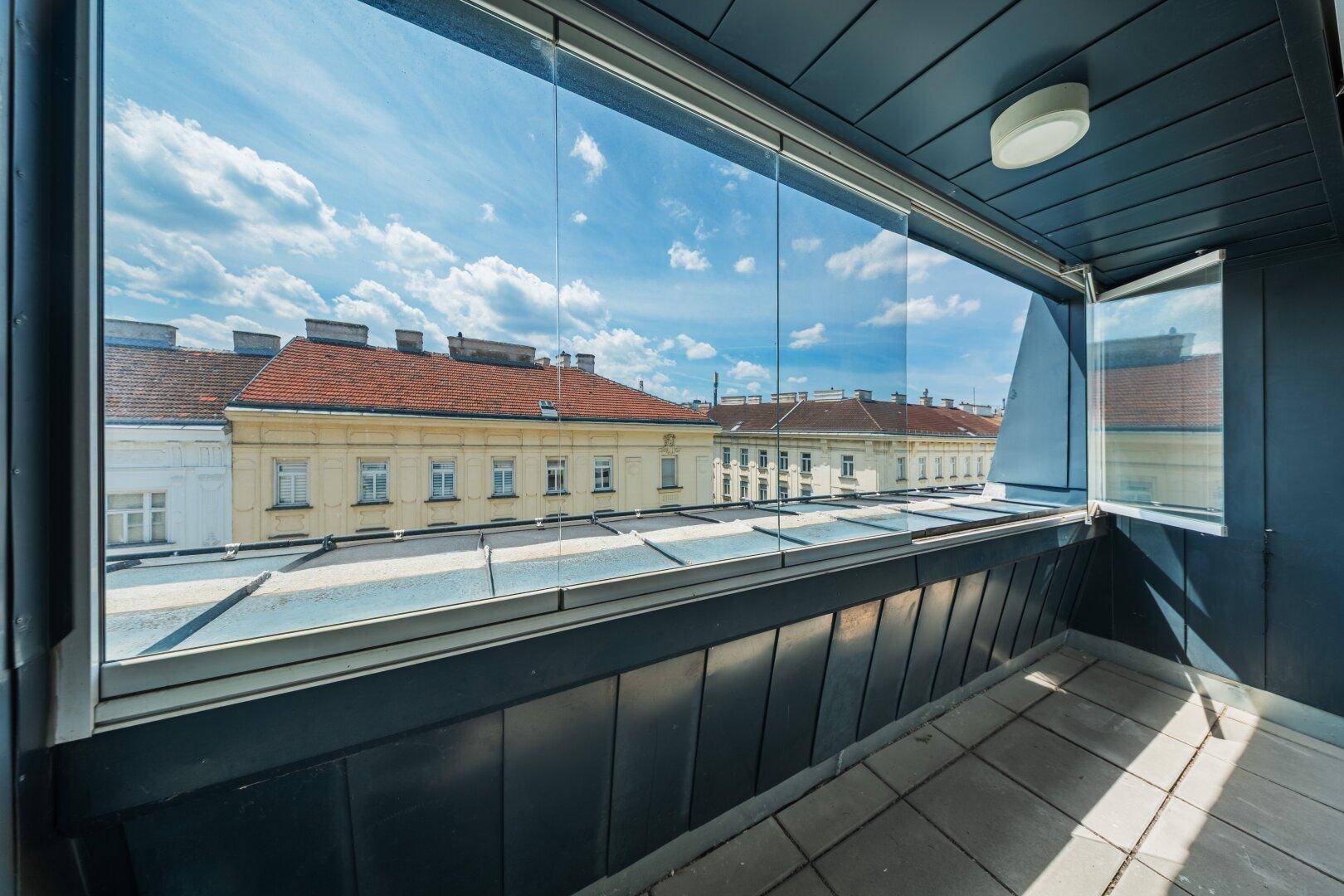 Verglaster Balkon mit Fliesenboden und Blick über die Dächer der Stadt.