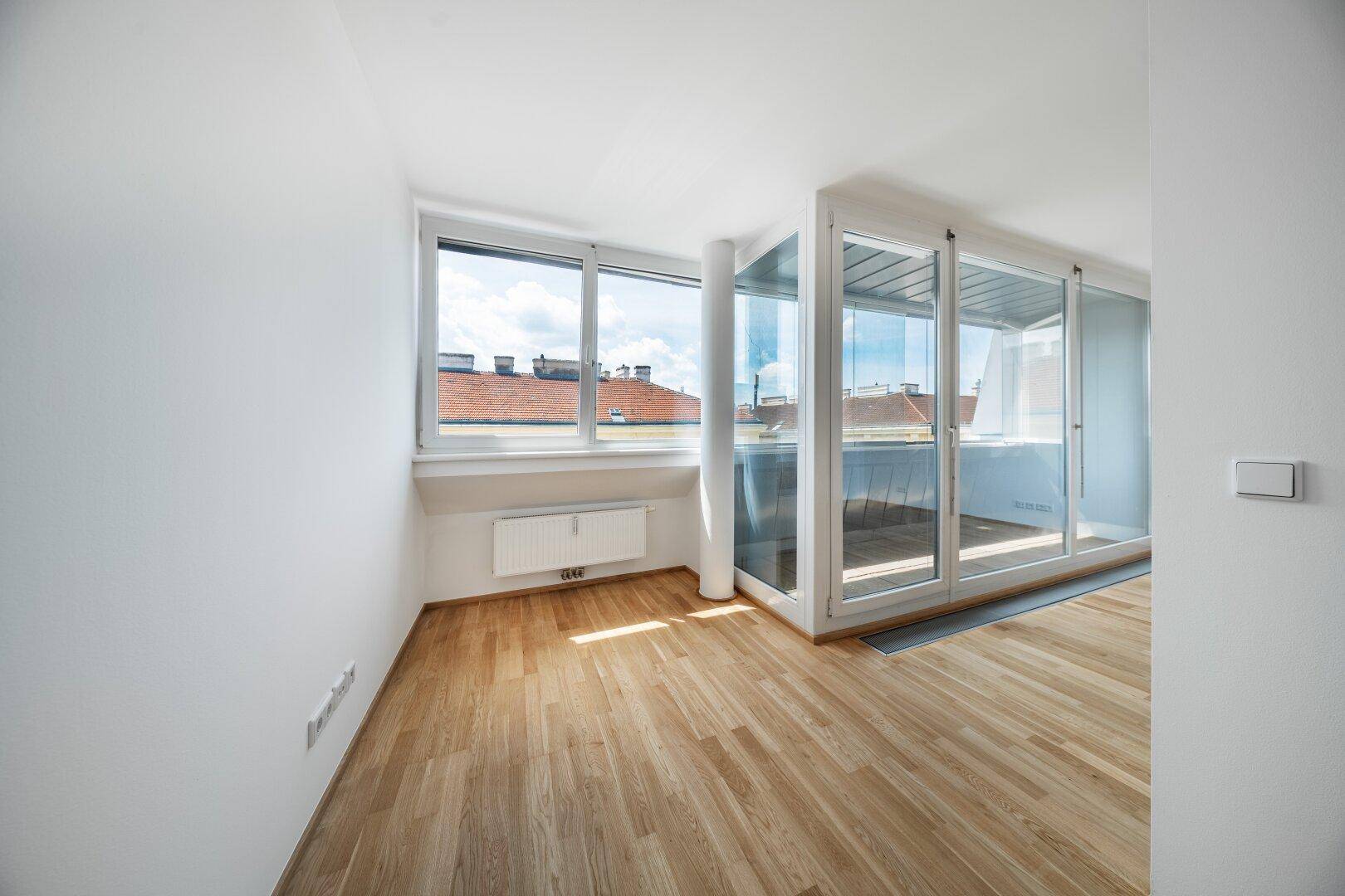Heller Wohnraum mit Holzboden und großen Fenstern, die einen weiten Blick bieten.