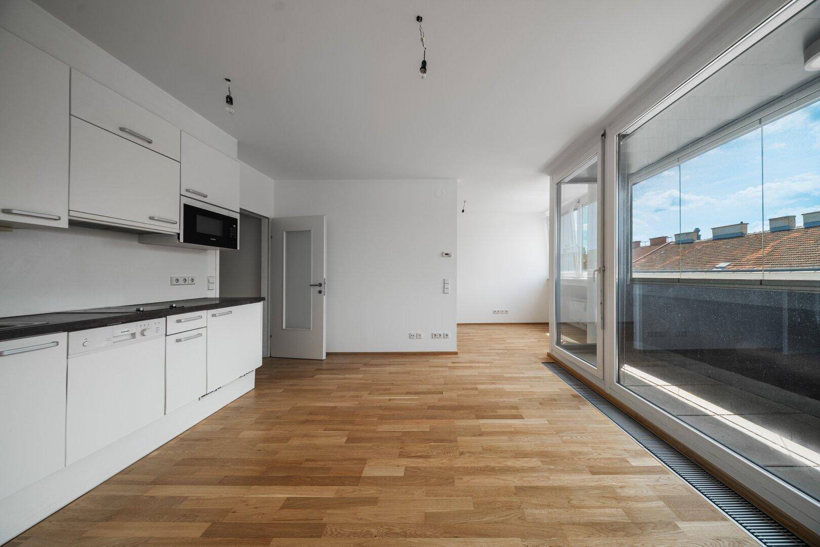 Heller Wohnbereich mit moderner Küchenzeile, Holzboden und Blick auf die Stadt.