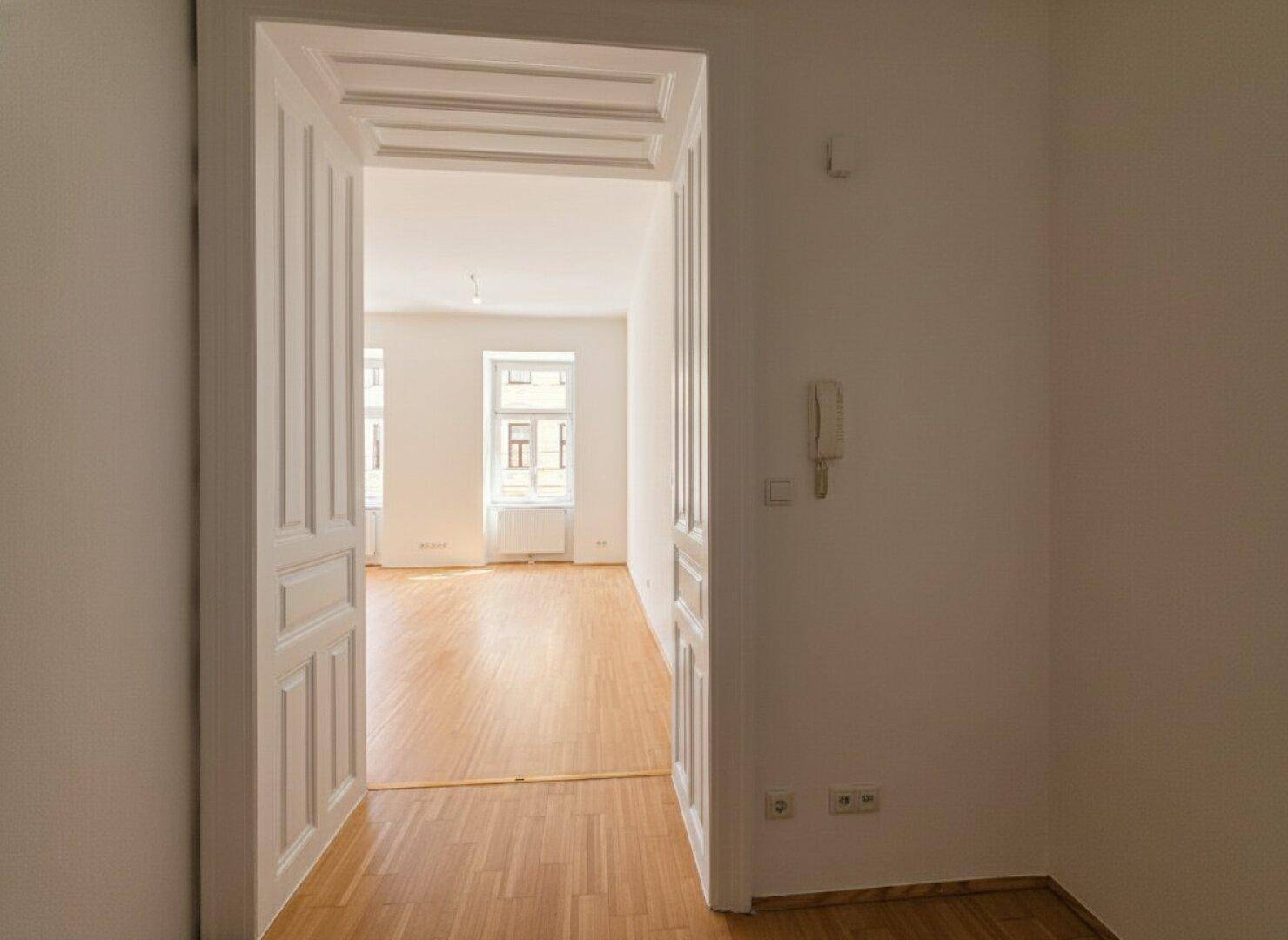 Heller Flur mit Parkettboden und einer eleganten Tür, die in einen weiteren Wohnbereich führt.