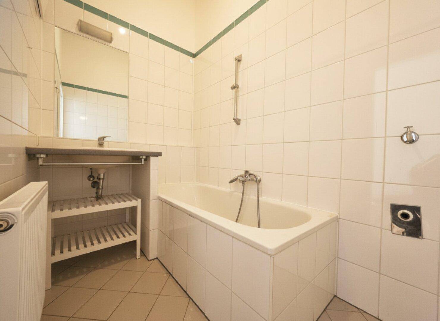 Gefliestes Badezimmer mit Badewanne, Waschbecken und Spiegel, in einem gepflegten Zustand.