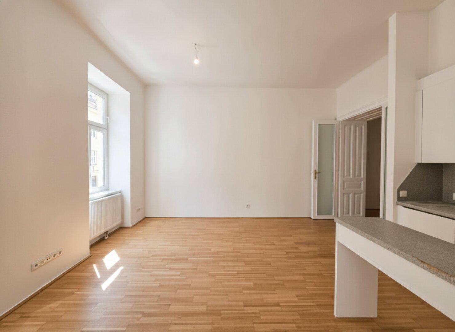 Offener Wohnbereich mit Parkettboden und viel Tageslicht, verbunden durch eine moderne Küchentheke.