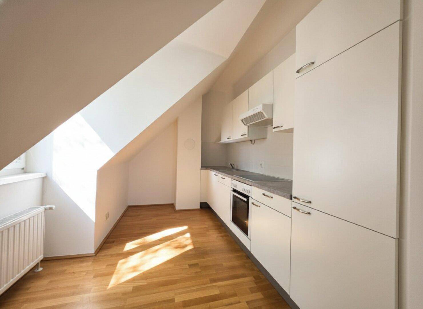 Moderne Küche im Dachgeschoss mit weißen Einbauschränken, Herd und Holzboden unter schrägen Wänden.