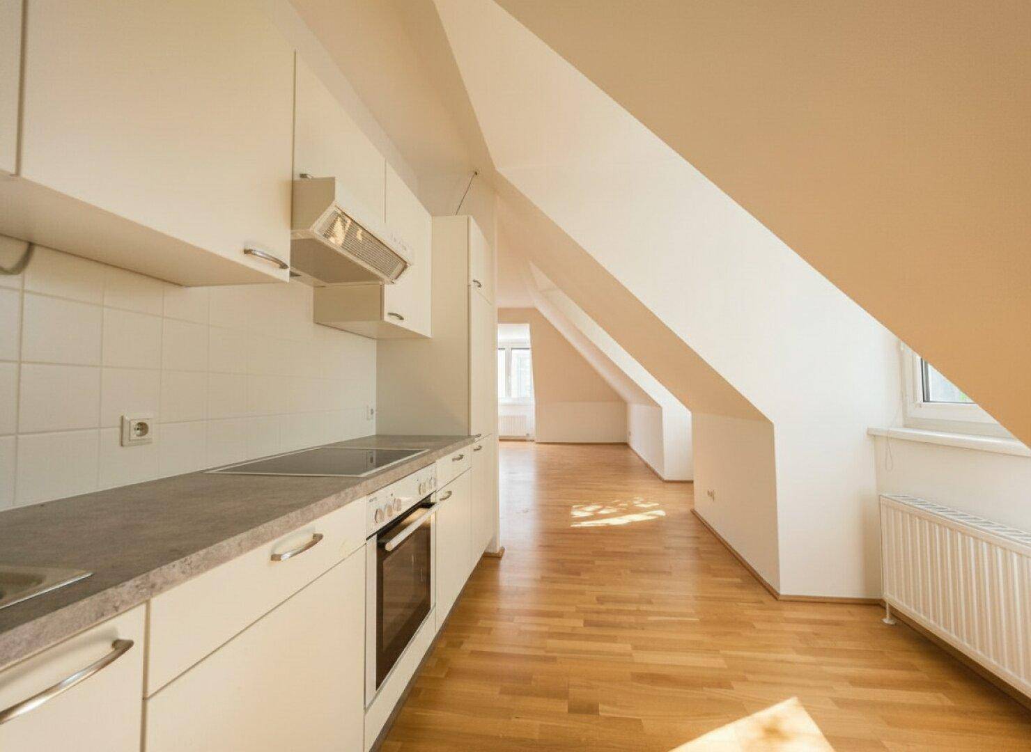 Helle Dachgeschossküche mit weißen Schränken, Arbeitsplatte und Blick in den angrenzenden Wohnbereich.