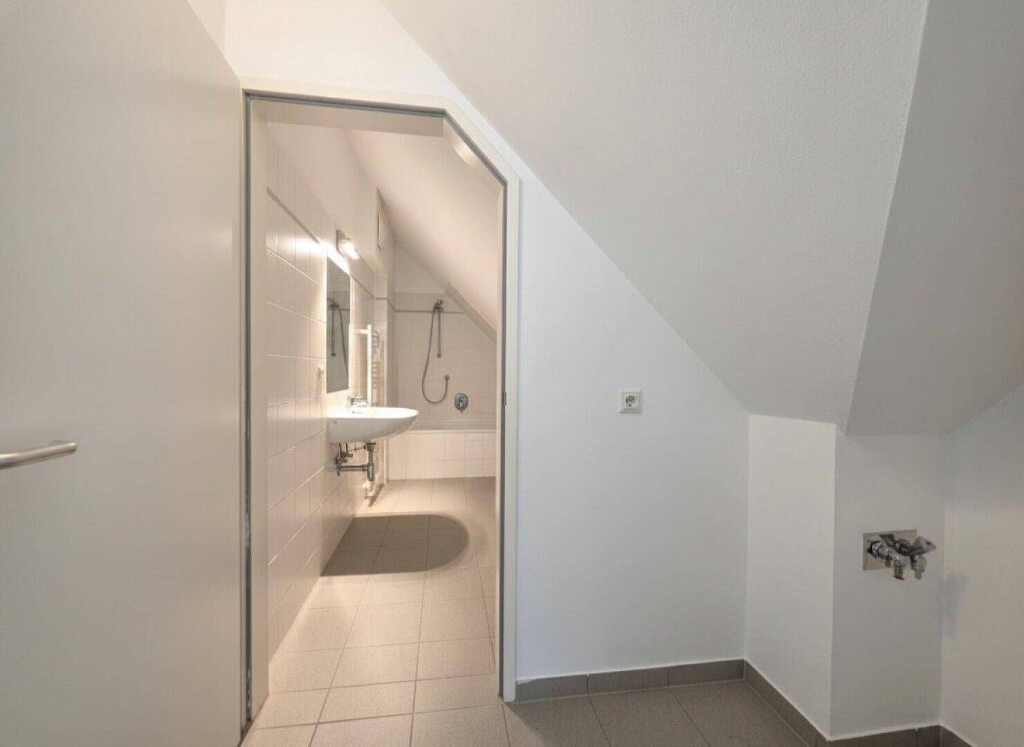 Heller Flur mit Zugang zu einem Badezimmer, das mit weißen Fliesen und einer Badewanne ausgestattet ist.