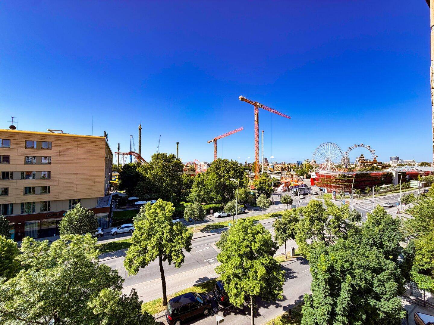 Weitläufiger Blick über die Stadt mit Straßen, Bäumen und dem Prater mit Riesenrad und Achterbahn.