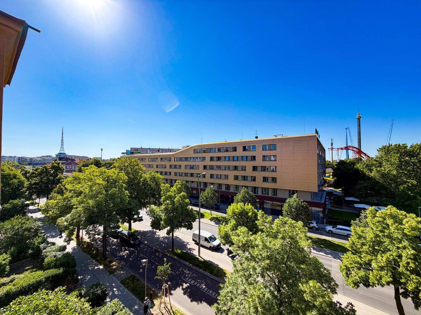 Blick von oben auf ein modernes Gebäude mit vielen Bäumen und einer belebten Straße unter blauem Himmel.