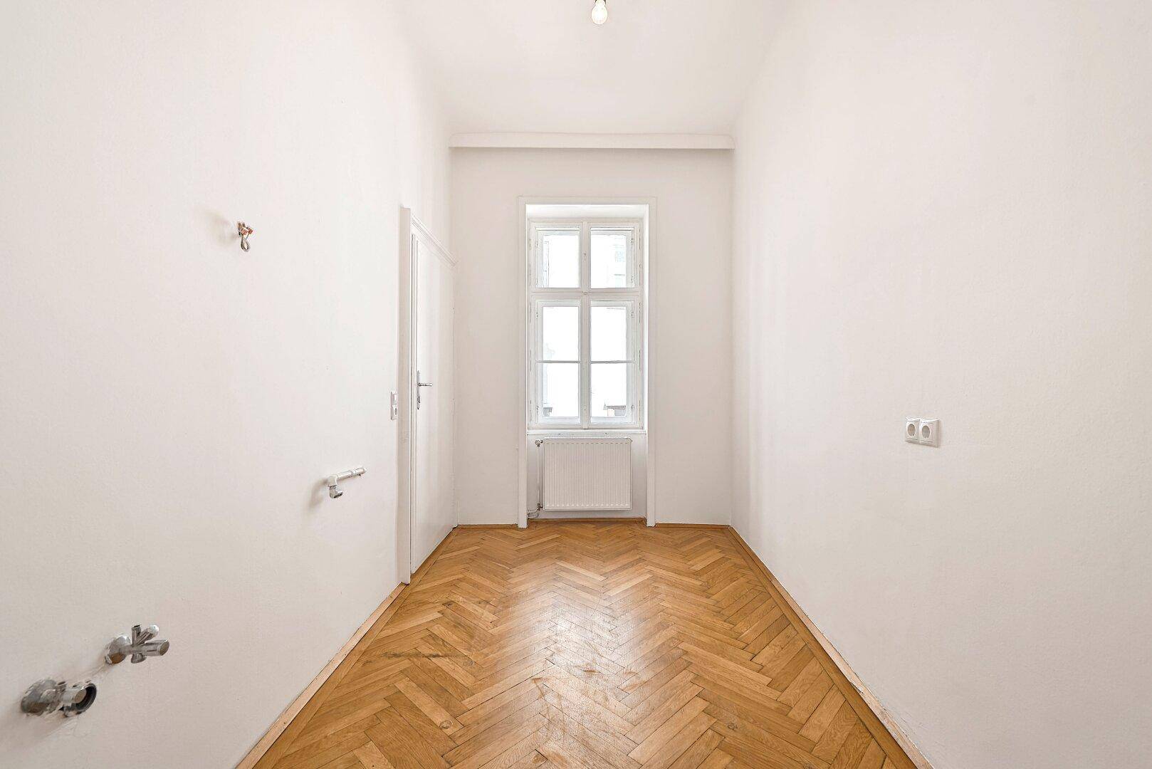 Langer, schmaler Raum mit Fenster und Fischgrätparkett, ideal als Flur oder Abstellraum.