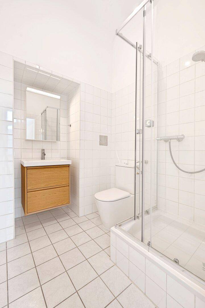 Modernes Badezimmer mit weißen Fliesen, Dusche und schwebendem Holzwaschtisch.