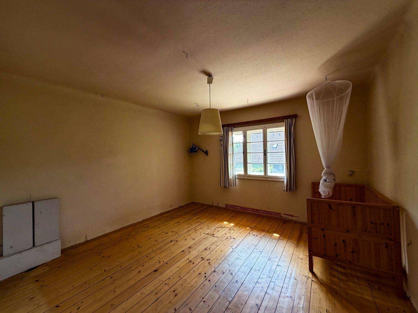 Helles Schlafzimmer mit Holzdielenboden und einem Kinderbett, bereit zur individuellen Gestaltung.