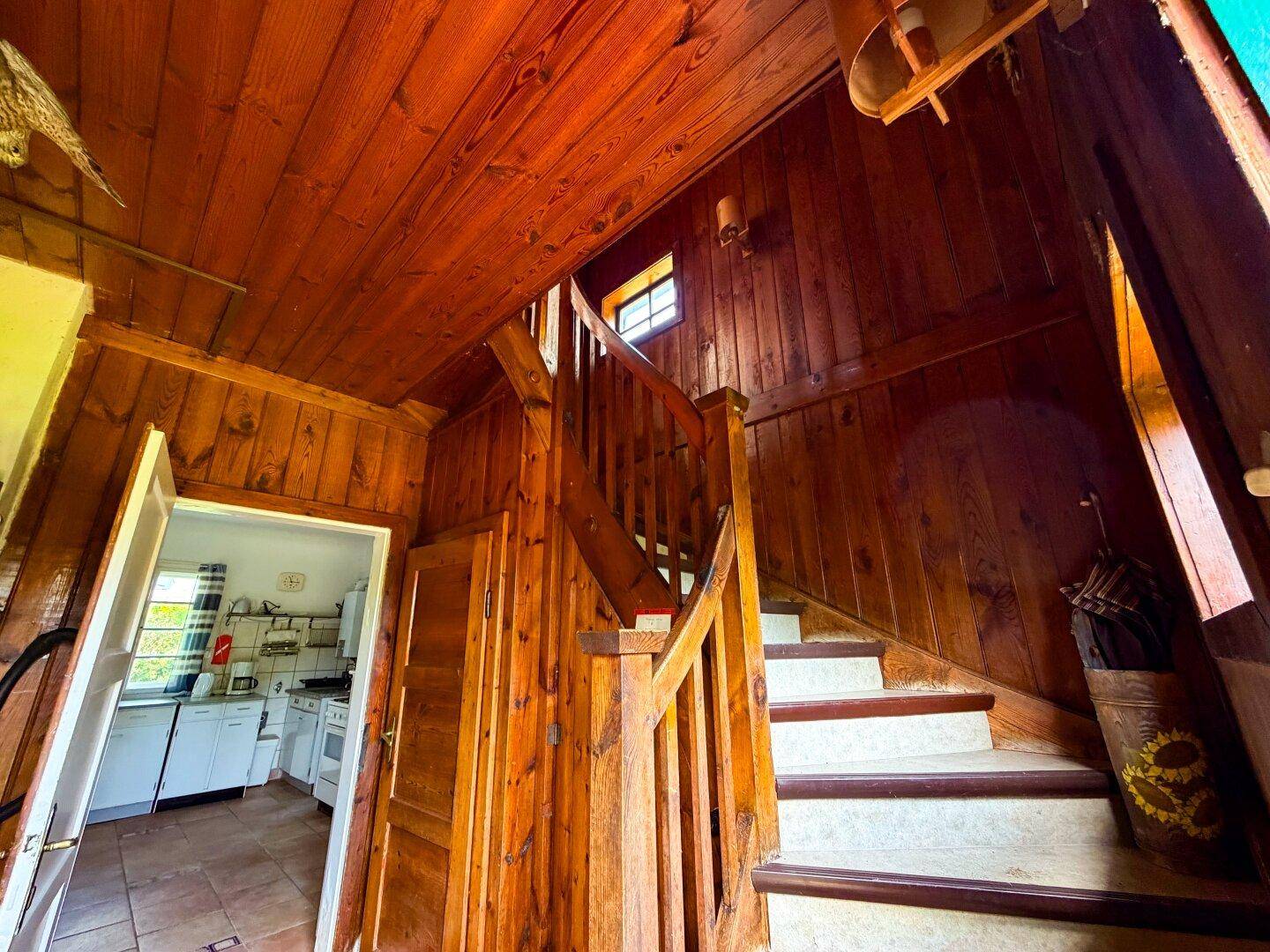 Detailansicht der Holztreppe und des Flurs mit rustikaler Holzvertäfelung und natürlichem Licht.