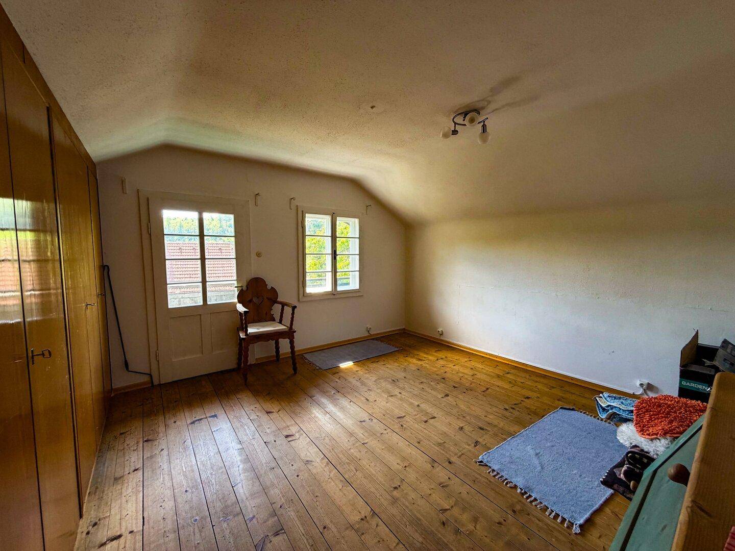 Geräumiges Schlafzimmer im Dachgeschoss mit Holzdielenboden, Dachschräge und zwei Fenstern.