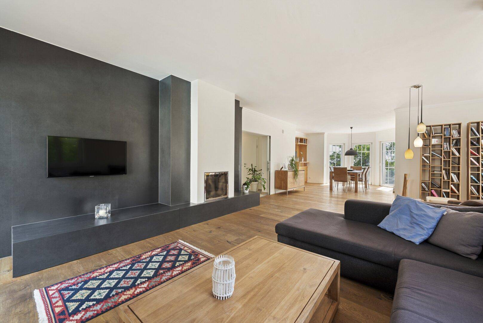Moderner Wohnbereich mit dunkler Akzentwand, Kamin und Holzboden, offen zum Essbereich.