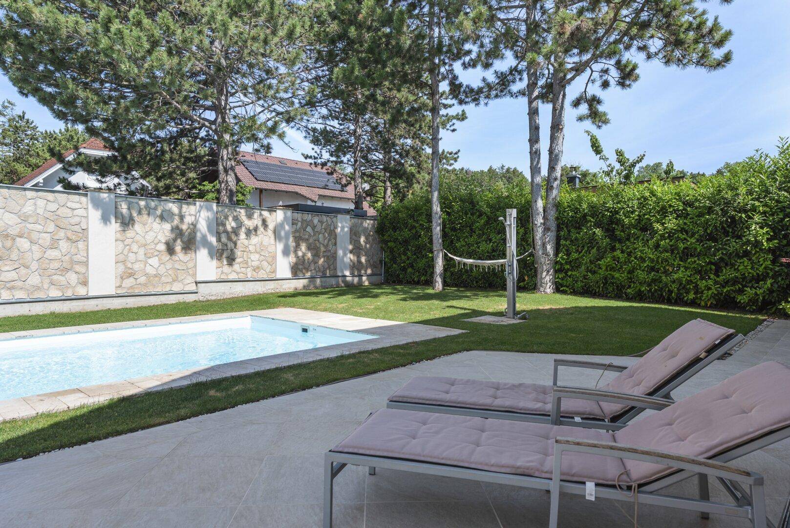 Entspannungsbereich im Garten mit Pool, Liegestühlen und einer hohen Hecke als Sichtschutz.