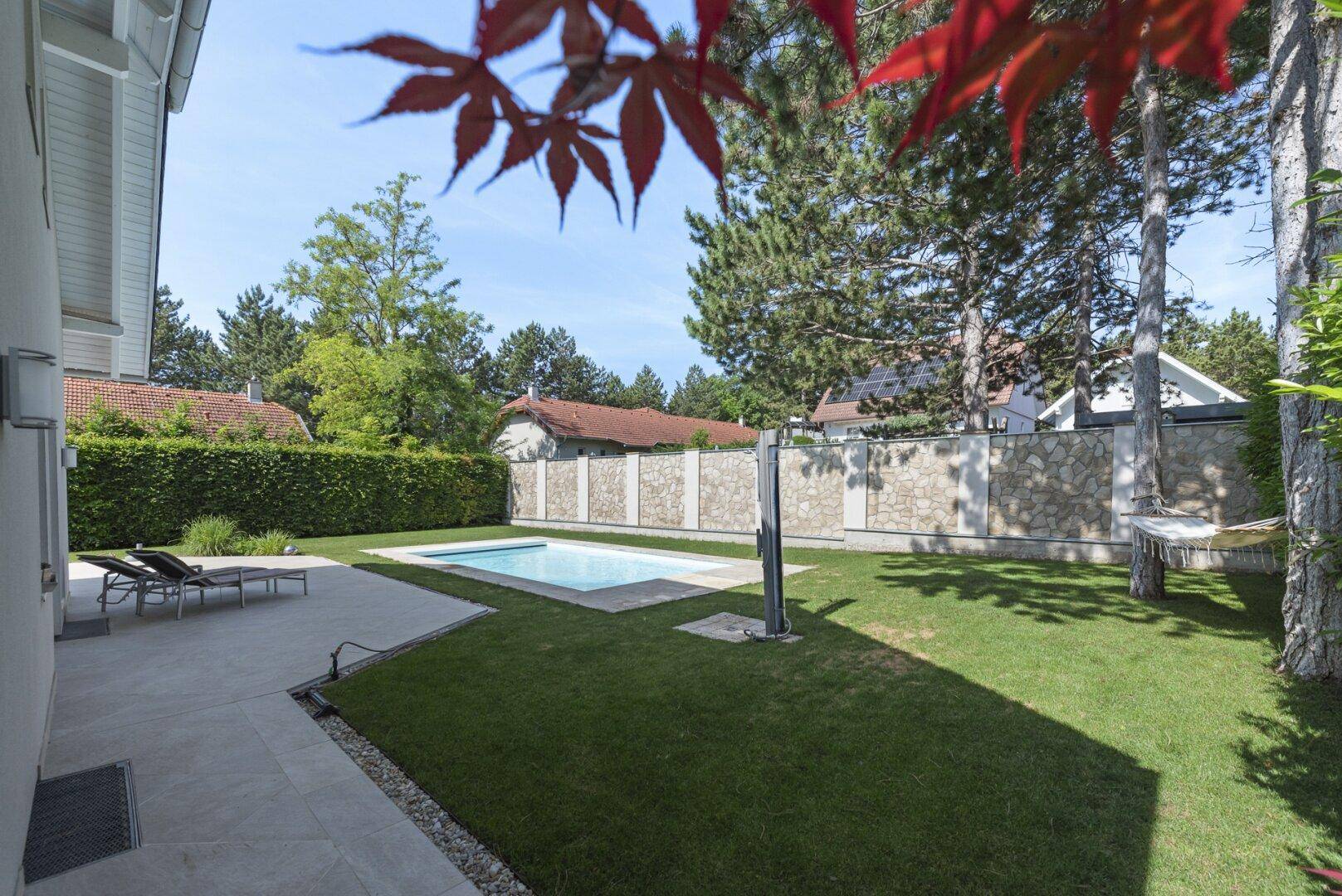 Weitläufiger Garten mit Pool, Liegewiese und umgebender Bepflanzung unter blauem Himmel.